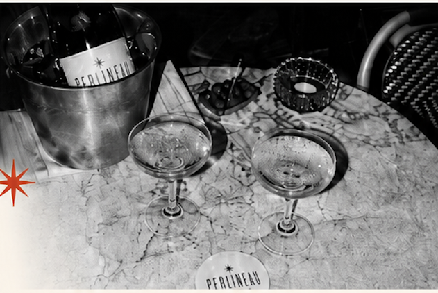 Black and white photograph of a Perlineau bottle in an ice bucket with two coupe glasses on a marble café table