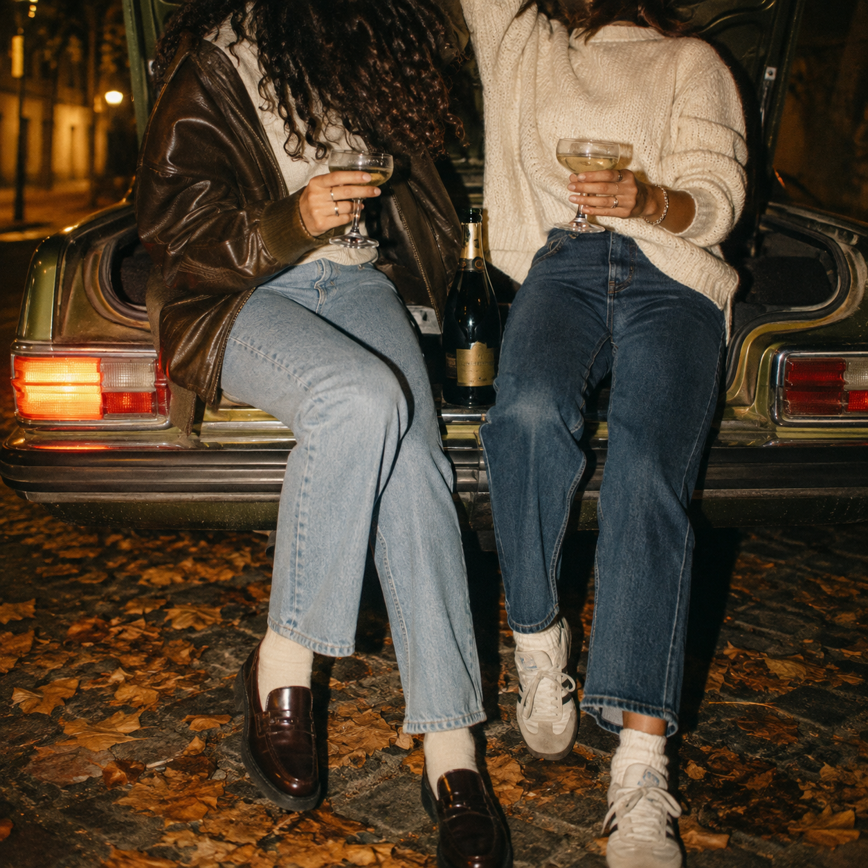 Black and white photograph of two friends sitting on the back of a car sharing a bottle of Perlineau